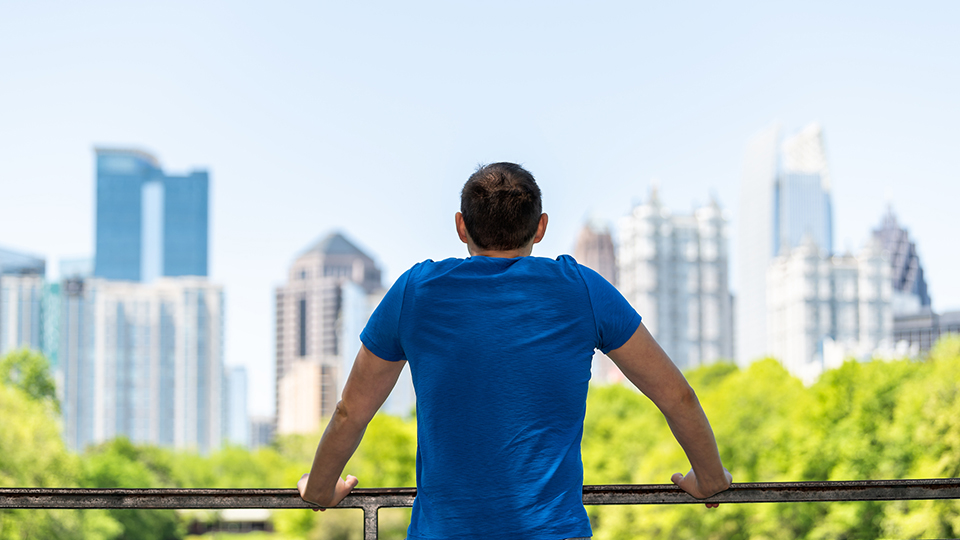 Young man standing leaning on railing in Piedmont Park in Atlanta, Georgia with scenic cityscape skyline of urban city skyscrapers downtown, Lake Clara Meer